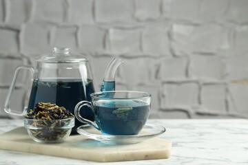 Delicious butterfly pea flower tea on white marble table against light background, space for text