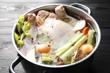 Whole raw turkey, cut onion, celery and spices in pot on black wooden table, closeup