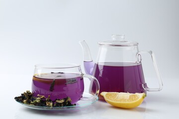 Delicious butterfly pea flower tea in glass cup, lemon, teapot and dry petals on white table