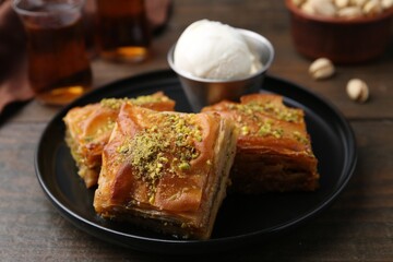 Delicious baklava with crushed nuts and ice cream on wooden table, closeup