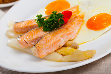 Hearty breakfast of fried eggs with salmon and steamed asparagus garnished with tomatoes and fresh greens..