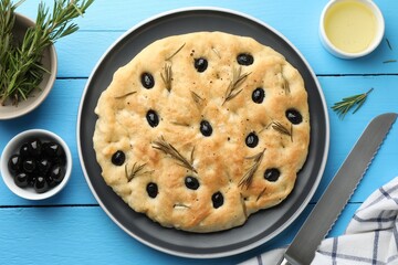 Delicious focaccia bread with olives, rosemary and oil on light blue wooden table, flat lay