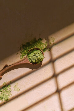 A wooden spoon filled with green matcha powder under the sunlight