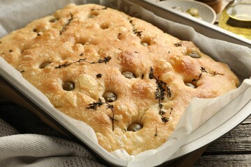 Delicious focaccia bread with olives and thyme on wooden table, closeup
