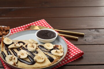 Delicious crepes with chocolate sauce, banana and almonds served on wooden table. Space for text
