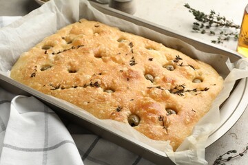 Delicious focaccia bread with olives and thyme in baking dish on table, closeup