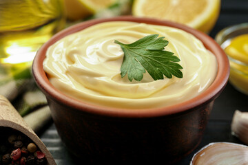 Delicious mayonnaise sauce with parsley in bowl, peppercorns and garlic on black table, closeup