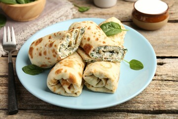 Tasty rolled crepes with cottage cheese and spinach served on wooden table, closeup