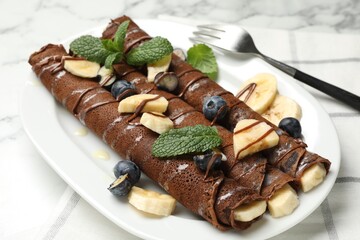 Delicious chocolate crepes with banana and blueberries served on white marble table, closeup