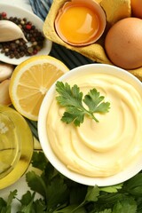 Delicious mayonnaise sauce with parsley in bowl and ingredients on white wooden table, flat lay