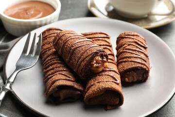 Delicious chocolate crepes with sweet paste and nuts on table, closeup