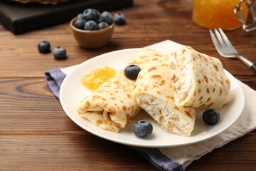 Delicious crepes with cottage cheese, jam and blueberries served on wooden table, closeup