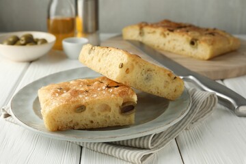 Pieces of delicious focaccia bread with olives, thyme, salt and knife on white wooden table, closeup