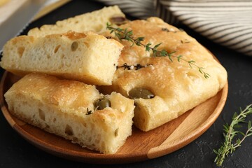Slices of delicious focaccia bread with olives, thyme and salt on black table, closeup