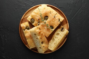Slices of delicious focaccia bread with olives, thyme and salt on black table, top view