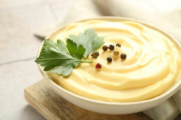 Delicious mayonnaise sauce with parsley and peppercorns in bowl on light table, closeup