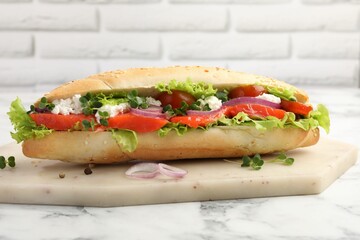 Delicious baguette with salmon on white marble table, closeup