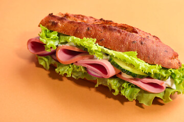 Baguette sandwich with ham on orange background, closeup
