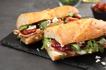 Halves of baguette sandwich with prosciutto and sun dried tomatoes on grey table, closeup