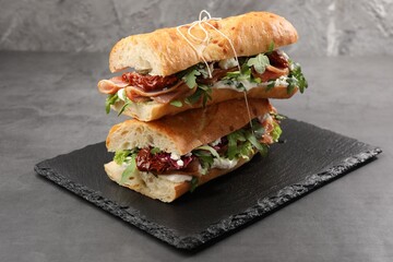 Halves of baguette sandwich with prosciutto and sun dried tomatoes on grey table