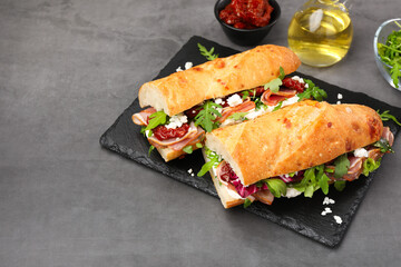 Halves of baguette sandwich with prosciutto and sun dried tomatoes on grey table