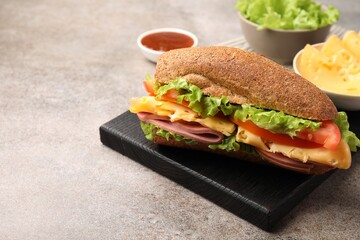 Delicious baguette sandwich with ham and ingredients on grey table