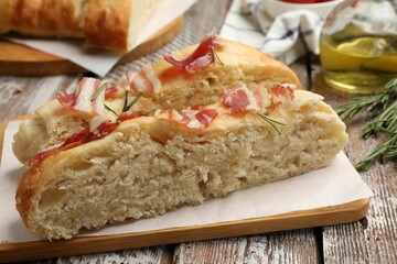 Slices of delicious focaccia bread with bacon and rosemary on wooden table, closeup