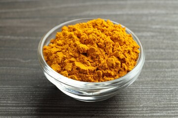 Turmeric powder in glass bowl on grey wooden table, closeup