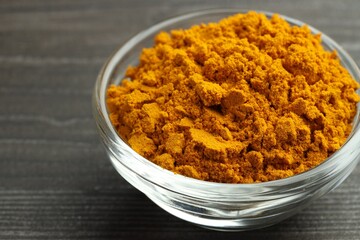 Turmeric powder in glass bowl on grey wooden table, closeup