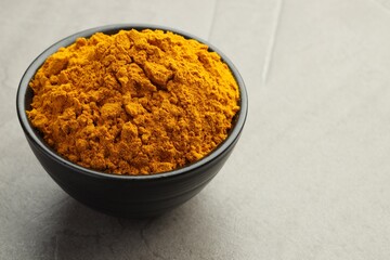 Turmeric powder in bowl on grey table, closeup. Space for text