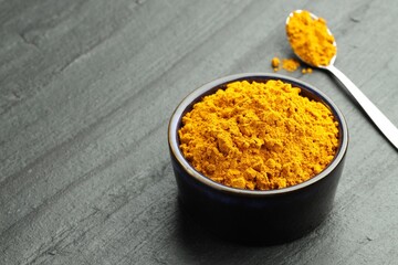 Turmeric powder in bowl and spoon on grey table, closeup. Space for text