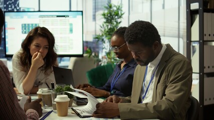 Fototapeta premium Shareholder examining infographics and resource allocation on tablet, gathering with associates for a strategy session. Utilizing data analytics to develop innovative solutions for growth. Camera B.