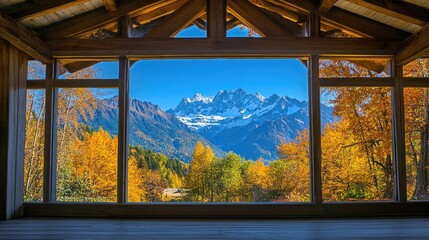 Fototapeta premium A stunning view of autumn colors and snowy peaks framed by a large window in a rustic house.