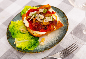Appetizing baked sandwich for breakfast or lunch with cream cheese spread, slices of tomatoes, mushrooms, onions, spicy chorizo sausage and parmesan seasoned with fragrant pesto served with lettuce ..