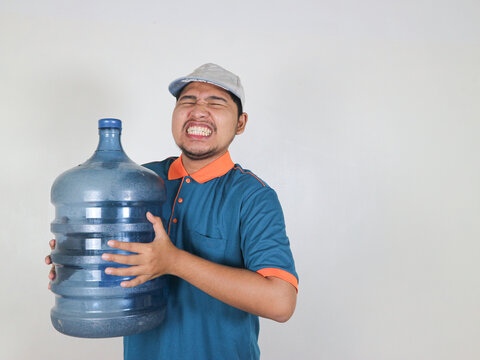 Asian delivery courier is carrying a gallon or big water bottle of mineral water with a pose of difficulty lifting the gallon he is holding