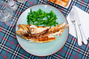 Halved grilled sea bass fish with fresh arugula on ceramic plate