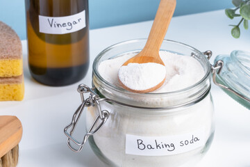 A jar filled with baking soda and a wooden spoon rests on a countertop alongside a bottle of vinegar and cleaning sponges. DIY cleaning method using natural products to remove stains. top view 