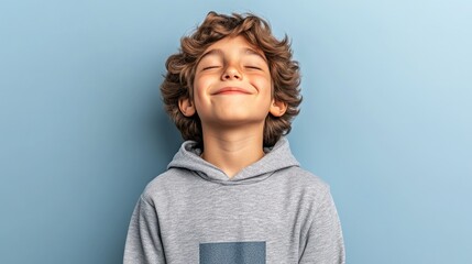 Happy caucasian young boy smiling in grey hoodie against blue background