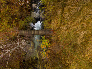 Fototapeta premium Wooden bridge over autumnal stream Aerial view