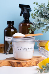 A jar filled with baking soda and a wooden spoon rests on a countertop alongside a bottle of vinegar and cleaning sponges. DIY cleaning method using natural products to remove stains. top view 