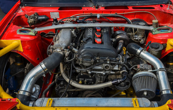 Detailed image of a heavily modified Nissan 200SX S13 sports car engine with visible components, set in a vibrant red chassis