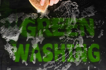 A female hand foam washes the Greenwashing message on a back background. Deception marketing and consumer manipulation. Creative concept of Greenwashing. 