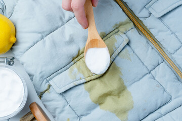 A person hand holding wooden spoon powder with baking soda on a yellow stain on clothing. DIY...