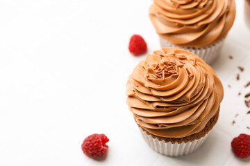 Tasty cupcakes with chocolate cream and raspberries on white tiled table, closeup. Space for text
