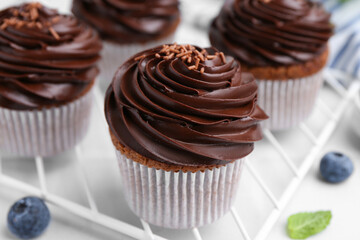 Tasty cupcakes with chocolate cream and blueberries on white tiled table, closeup