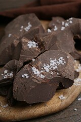 Pieces of chocolate with salt on wooden table, closeup