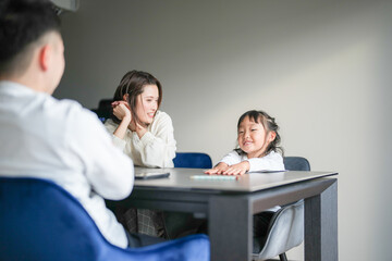 A Japanese parent and child, a woman in her 30s, a man in his 20s, and a 6-year-old girl, are studying at a table in their living room.