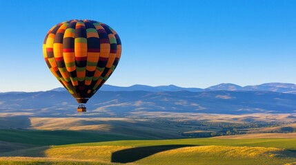 A colorful hot air balloon floats over rolling green hills and mountains.