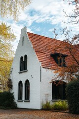 Charming white house with red roof surrounded by autumn foliage in a tranquil neighborhood under a cloudy sky in late afternoon