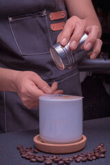 A woman barista operates a coffee brewing machine, pouring cinnamon into a cup of cappuccino coffee.